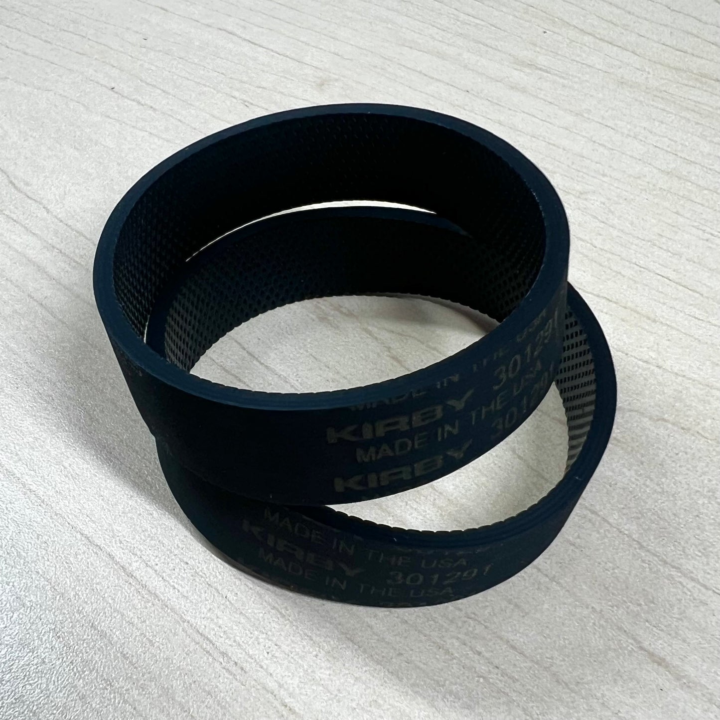 Two Kirby vacuum belts on flat surface.