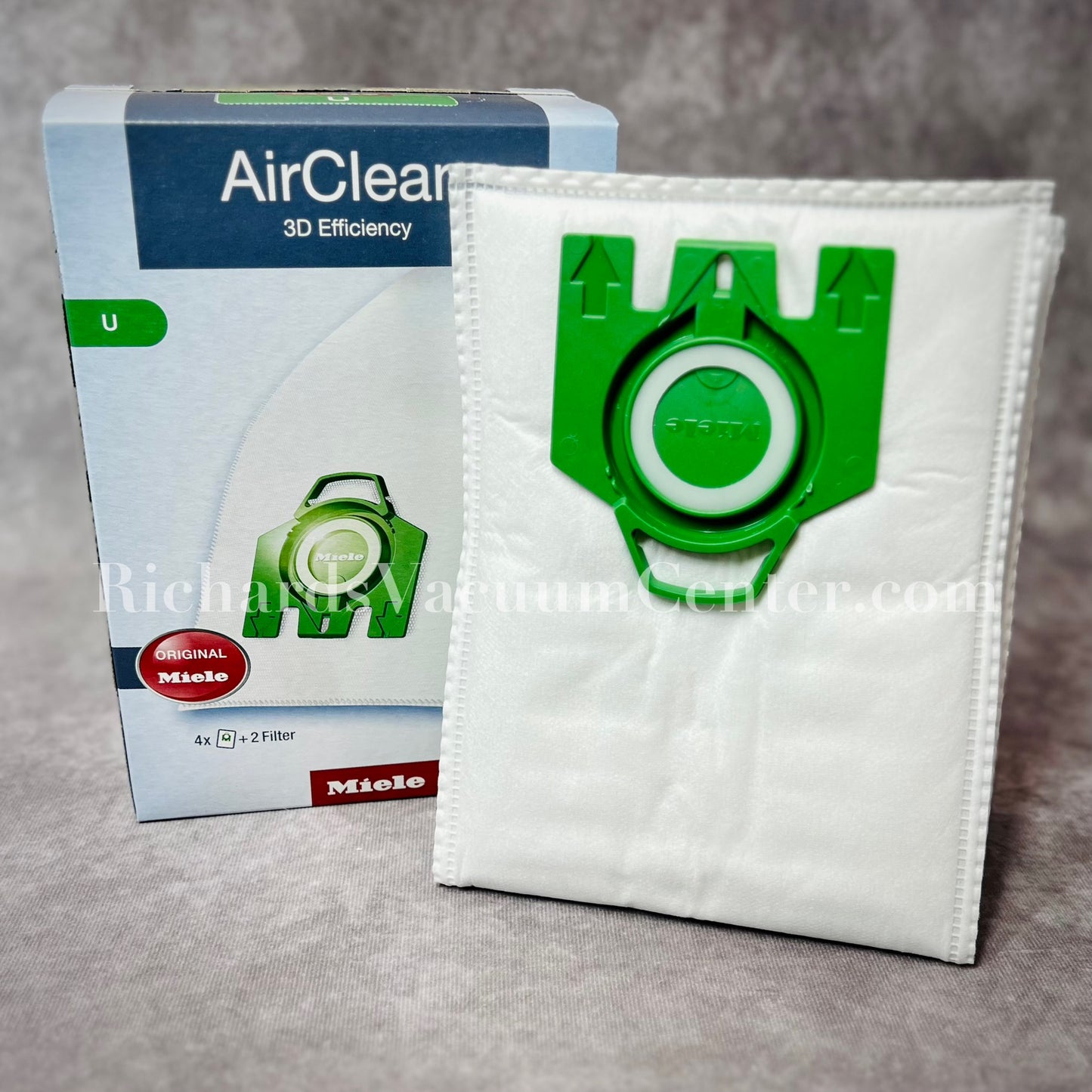A package of white Miele AirClean 3D Efficiency U type vacuum bags with green detailing, including one bag visible in front of the box.