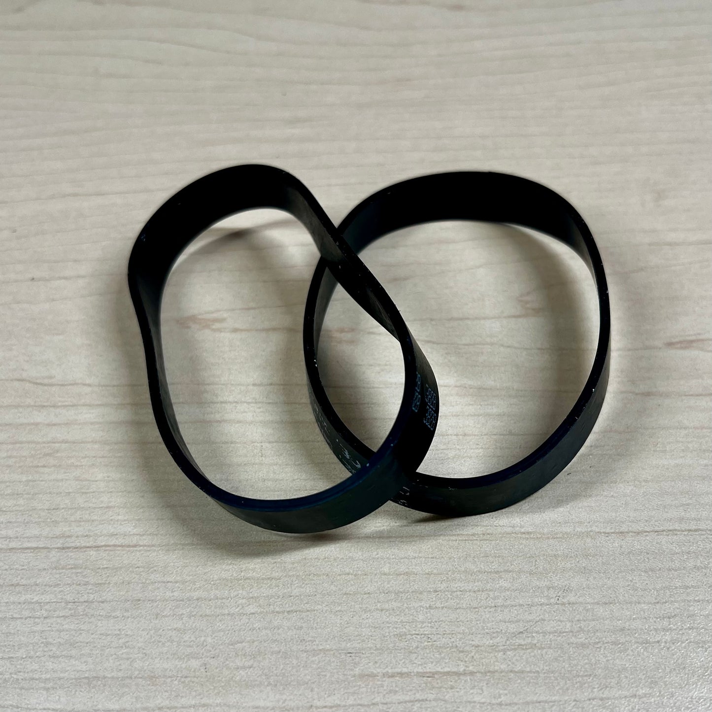 Two black vacuum belts sitting on flat surface.