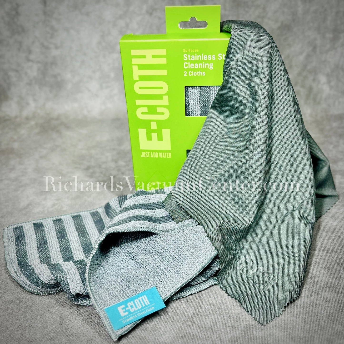 The image shows a stainless steel cleaning kit which includes a striped stainless steel cleaning cloth, a solid glass & polishing cloth, and their packaging with branding visible.