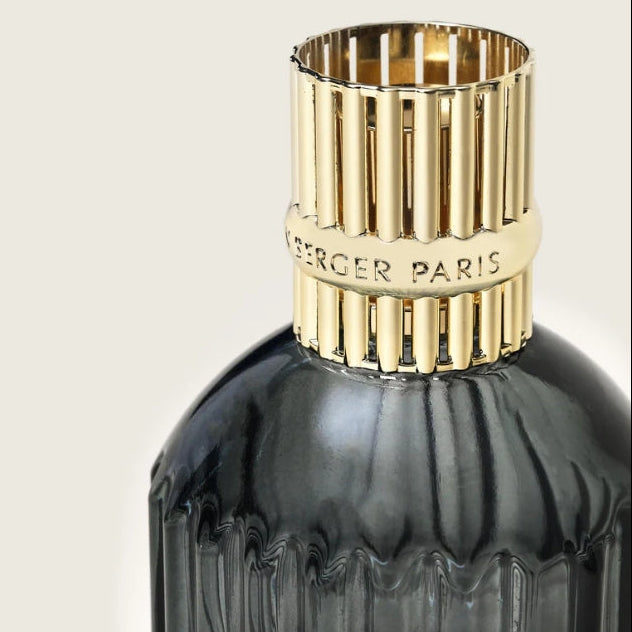 Home fragrance bottle with gold cap and dark glass body on a light gray background