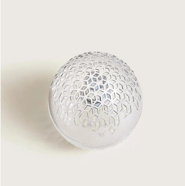 A spherical clear and silver Maison Berger lamp with a geometric honeycomb cutout pattern.