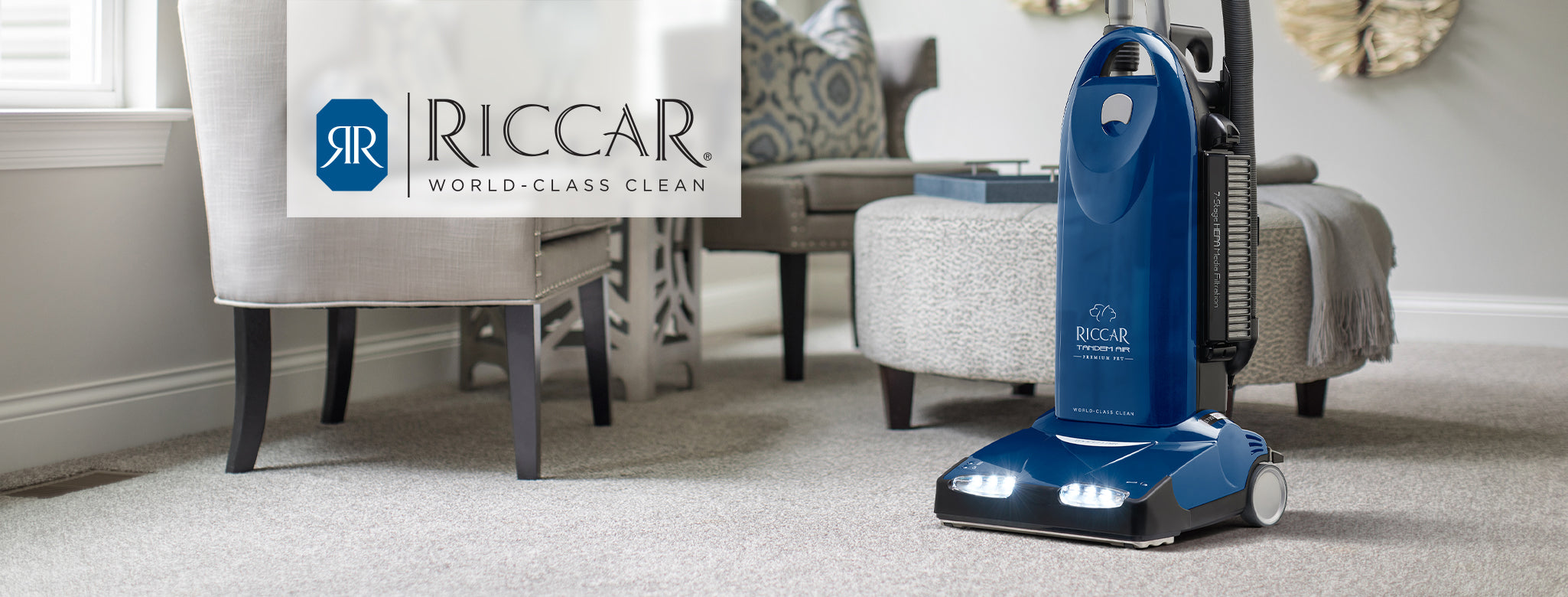 Blue Riccar R40 vacuum cleaner on a carpeted floor with a living room setting.