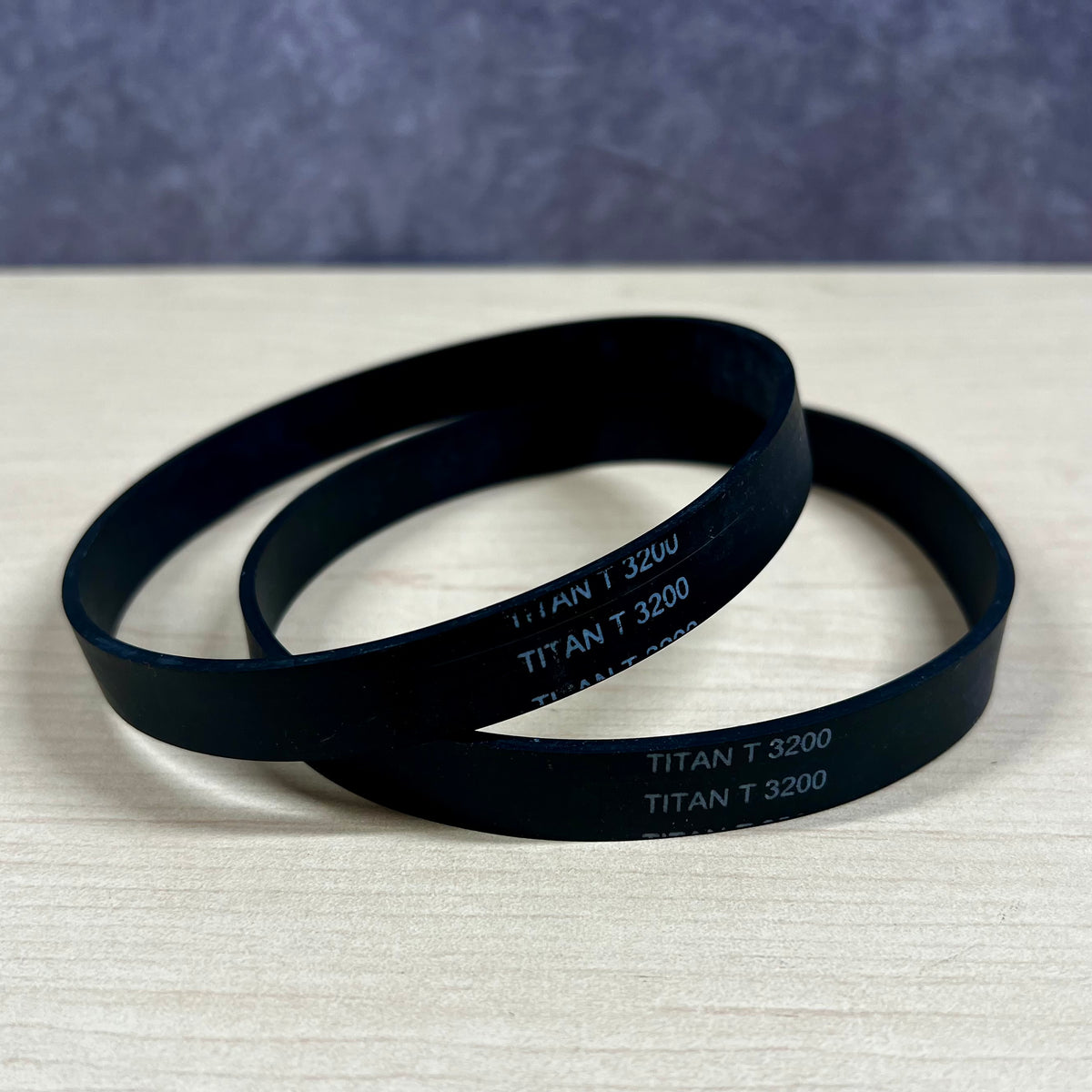 Two black belts labeled 'TITAN T 3200' on a textured surface with a blue gradient background.