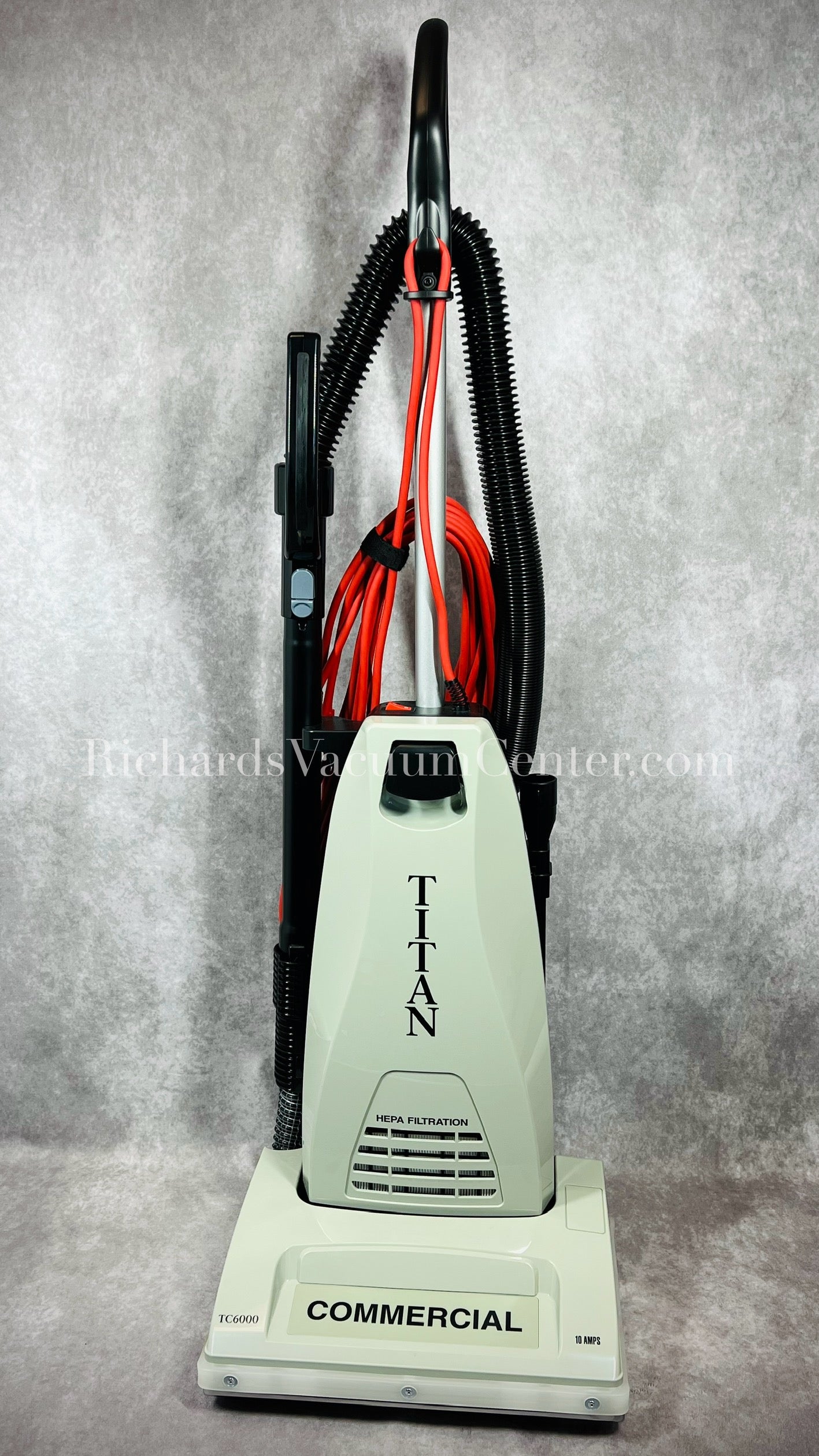 A Titan TC6000 Commercial upright vacuum cleaner in beige color with a metal handle and black accents. The vacuum has a clean air motor, telescopic wand, and on-board tools.