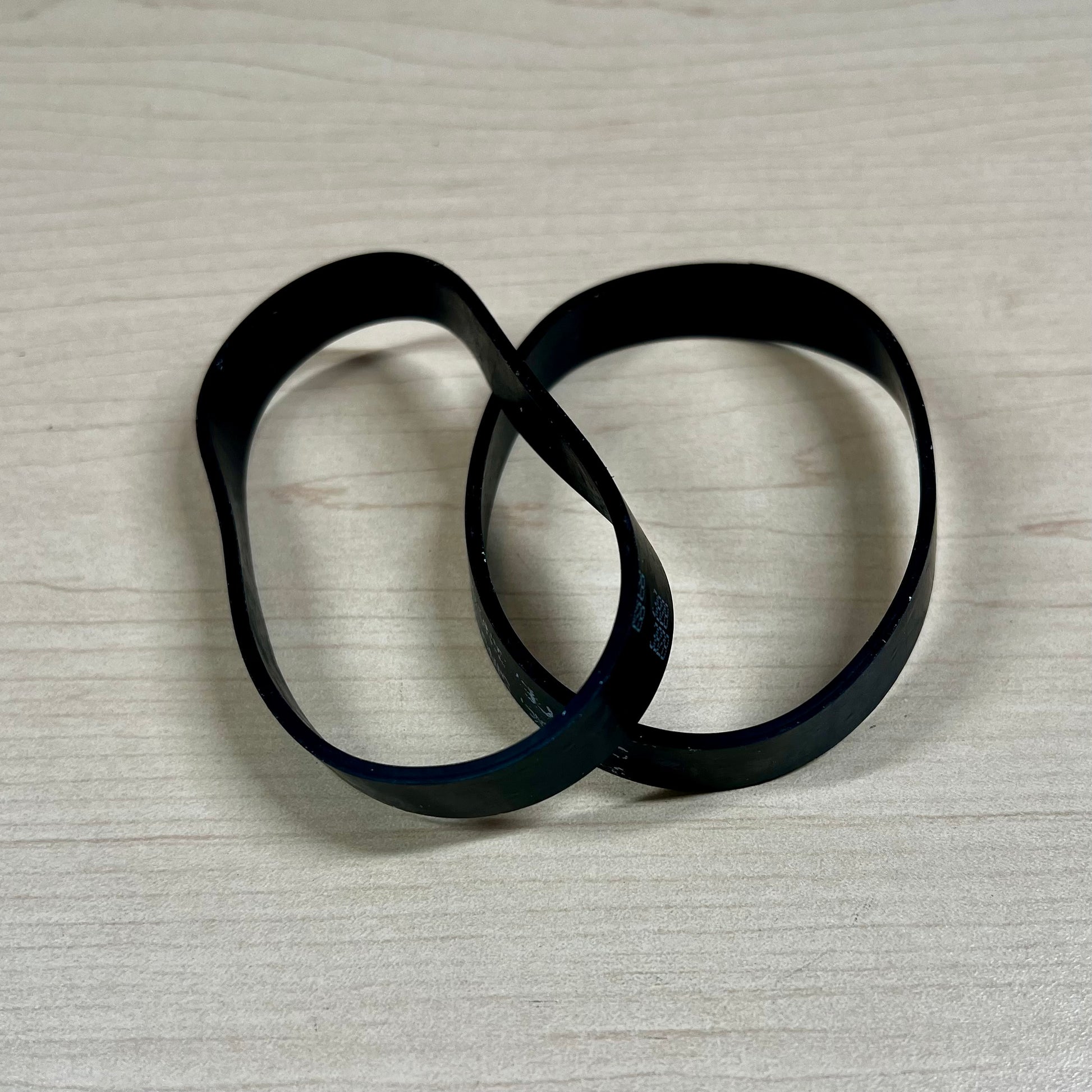 Two black vacuum belts sitting on flat surface.